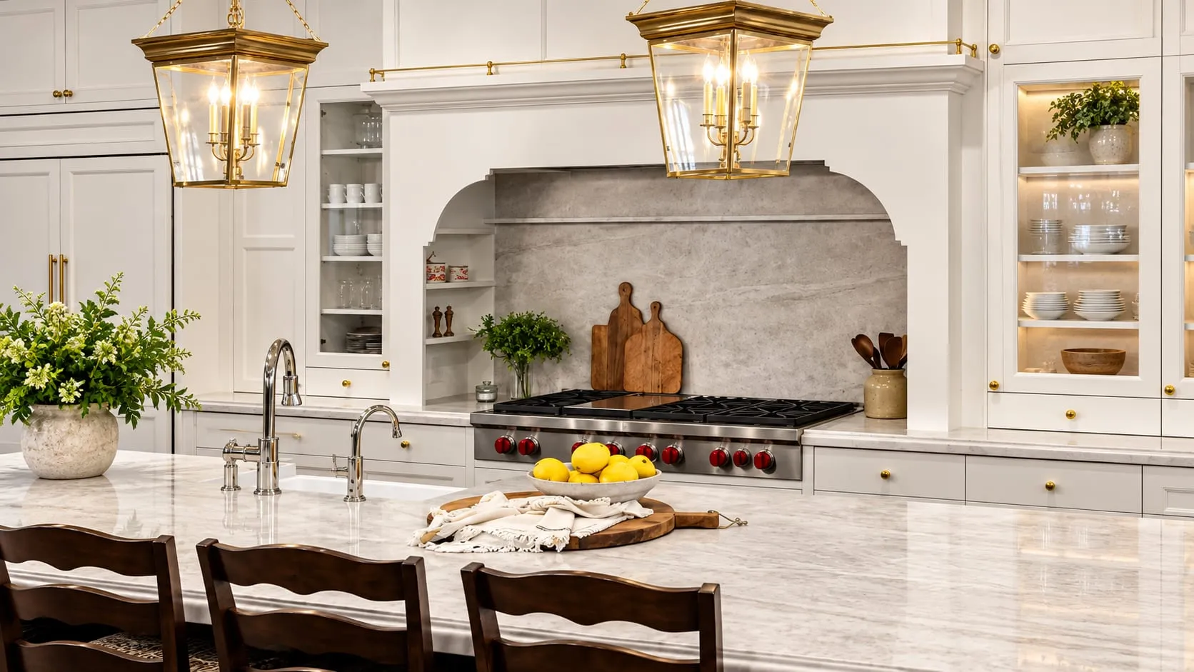 Classic white kitchen with a veined stone island, brass lantern pendants and a stone-framed range alcove