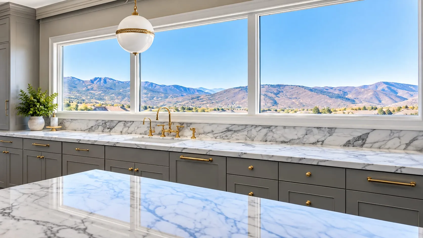 Kitchen with grey cabinets, grey-veined white stone countertops and a wide window onto hills